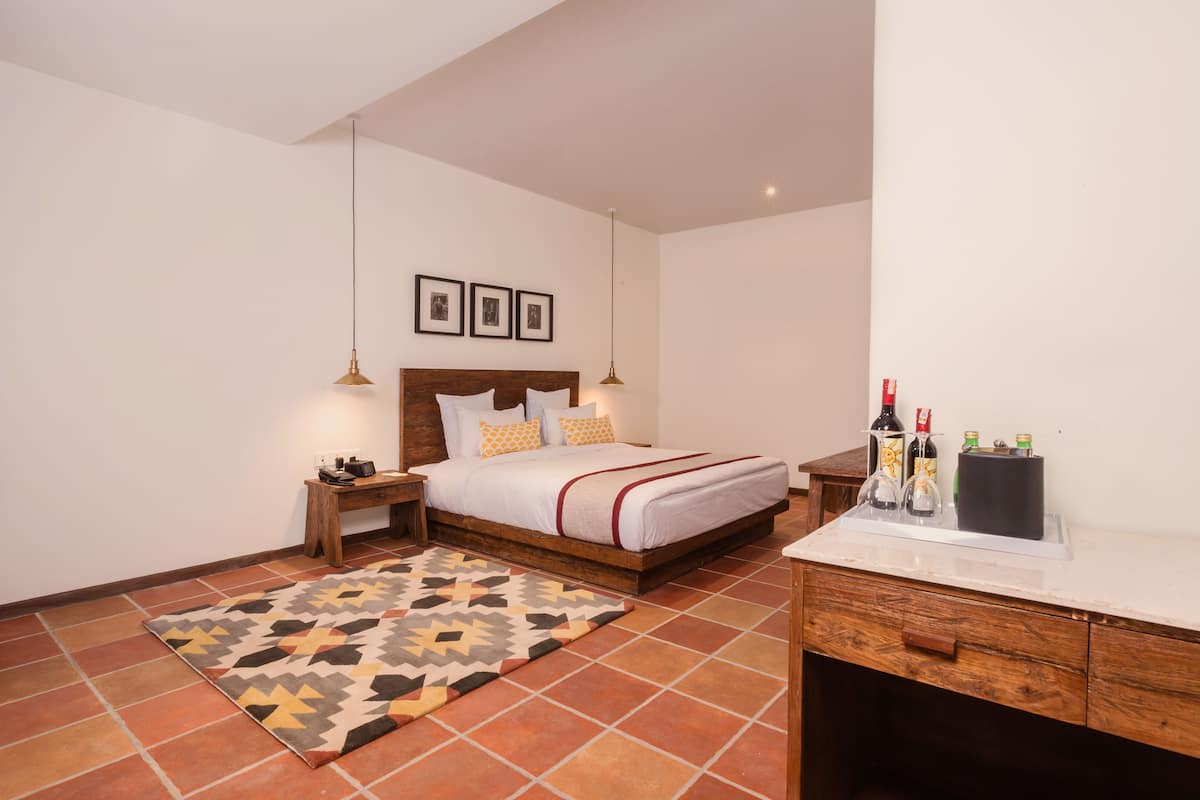 A bedroom with a bed, nightstands, a desk, a rug, and a minibar.