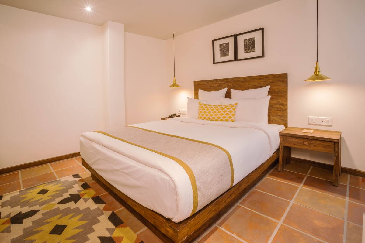 A neatly made bed with a wooden headboard, a bedside table with a lamp, and a patterned rug on the floor.