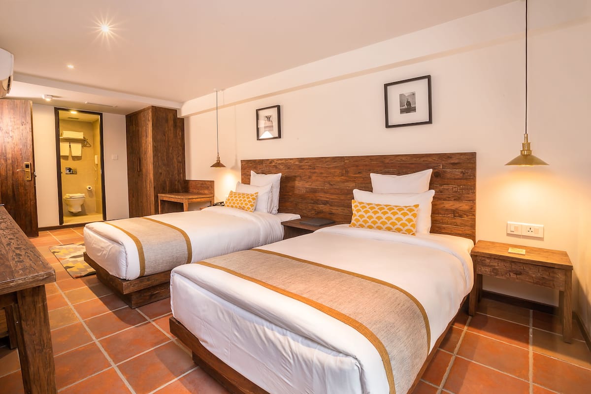 A hotel room with two beds, wooden headboards, white bedding, and a tiled floor.