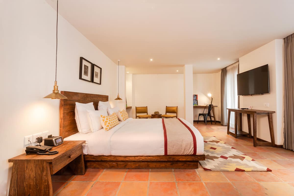 A hotel room with a large bed, bedside tables, a desk, a chair, a television, and a patterned rug.