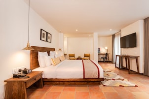 A hotel room with a large bed, bedside tables, a desk, a chair, a television, and a patterned rug.