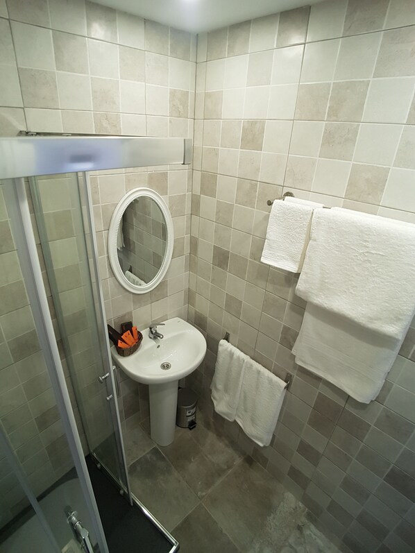 Un baño con cabina de ducha de vidrio, un lavabo con espejo y dos toallas blancas colgadas en la pared.