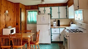 A compact kitchen with wooden cabinets, a refrigerator, a stove, and a dining table with chairs. - FISHING AND FAMILY FRIENDLY- NOTHING FANCY (Linesville)