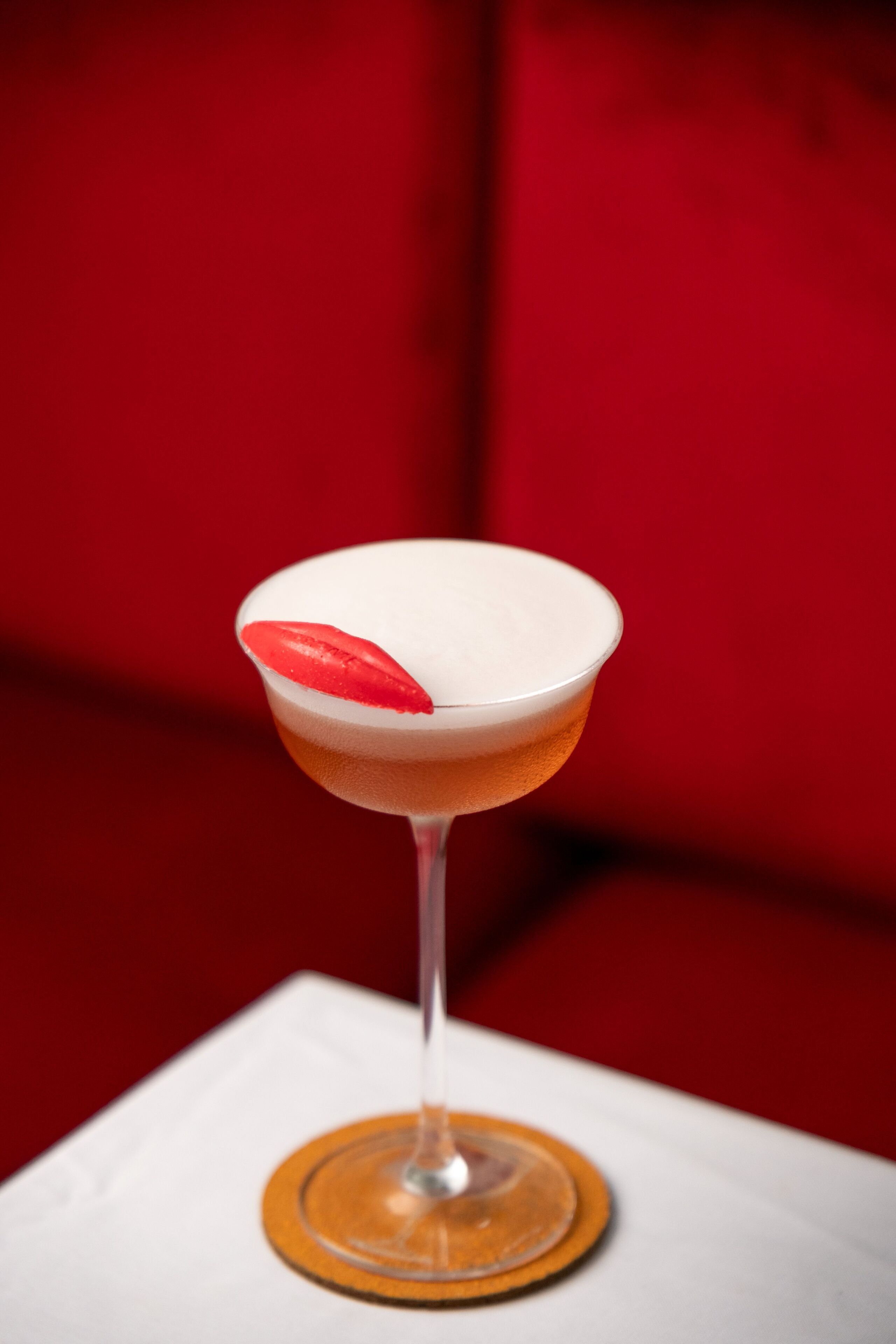 A martini glass with a red garnish on a white coaster, set against a red background.