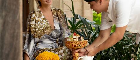 A person serving food to another person at an outdoor table with a decorative bowl and a white teapot.