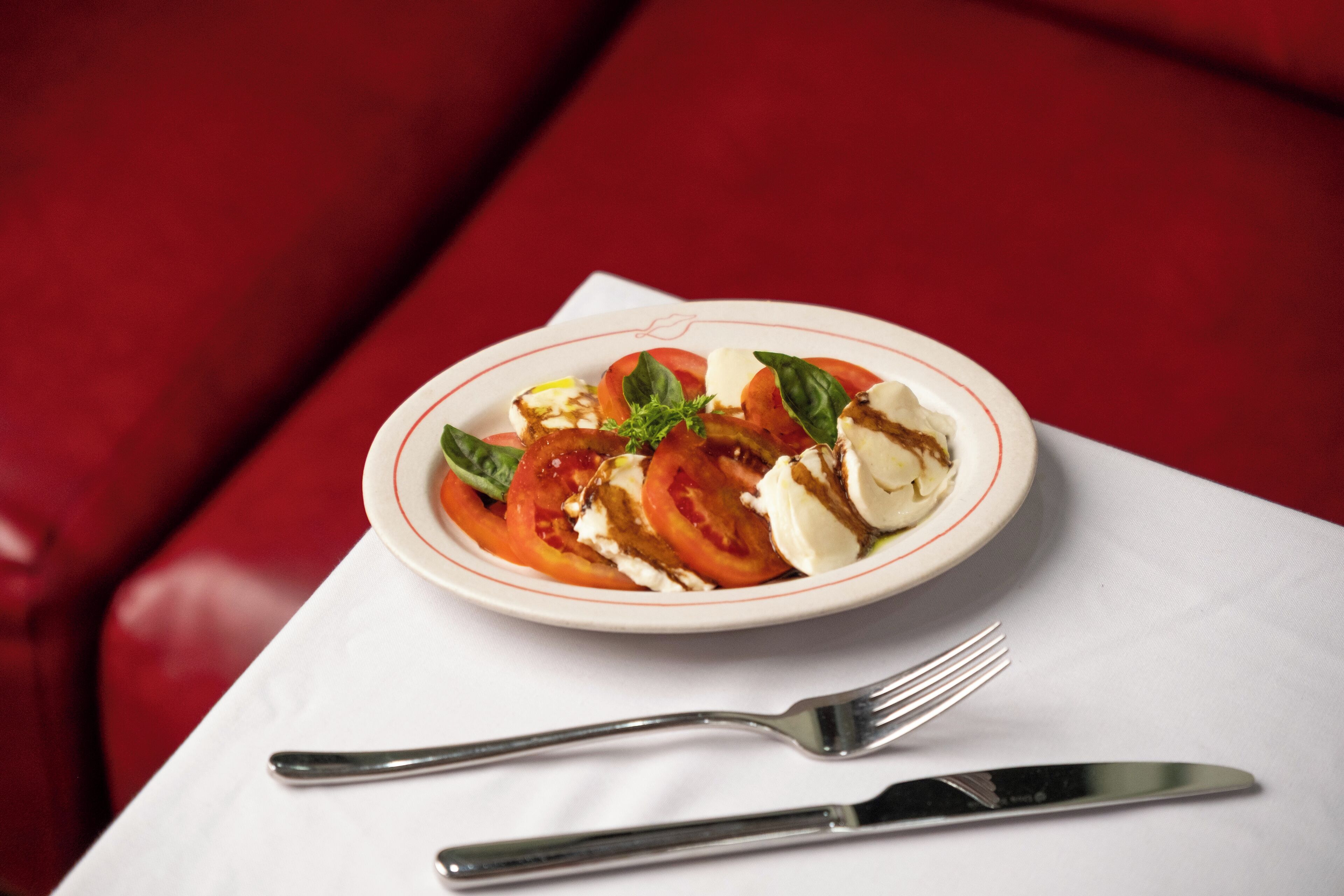 A plate of Caprese salad with tomatoes, mozzarella, and basil on a white plate.