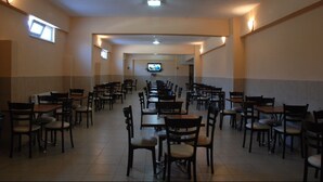 A spacious dining area with multiple tables and chairs, a television mounted on the wall, and a tiled floor. - Ustundag Otel (Keçiborlu)