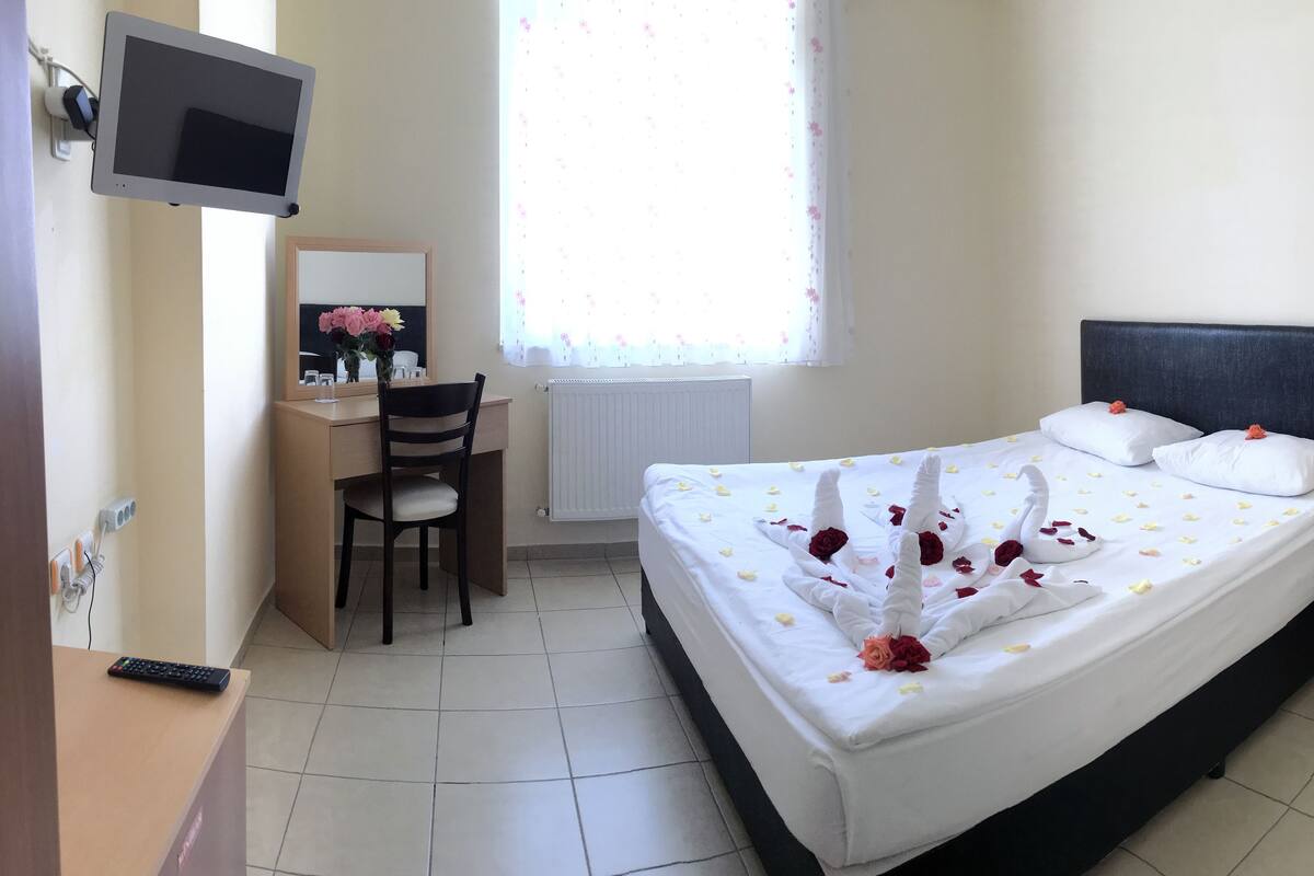 Une chambre d’hôtel avec un lit, un bureau, une chaise, un téléviseur fixé au mur et une fenêtre donnant sur l’extérieur.