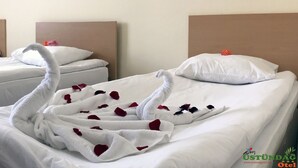 A hotel room with two beds, each adorned with a towel shaped like a swan and scattered with rose petals. - Ustundag Otel (Keçiborlu)