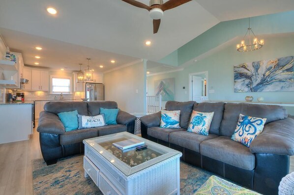 A spacious living room with two sofas, a coffee table, and a ceiling fan. - Experience oceanfront bliss at Blue Yonder, a spacious 4-bedroom retreat in Oak Island. (Oak Island)