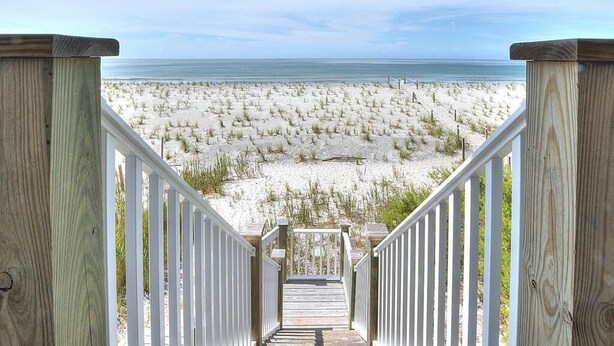 Eine Holztreppe führt zu einem Strand mit Blick auf den Ozean.