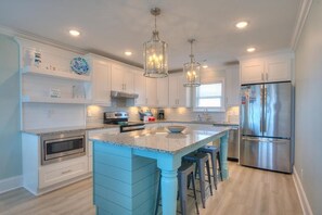A modern kitchen with white cabinets, a central island, stainless steel appliances, and pendant lighting.