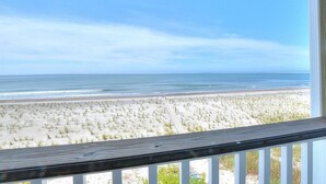 Blick auf einen Strand vom Balkon aus, mit Holzwertlauf, Sandstrand und Meer.