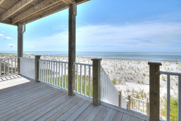 A wooden deck with white railings overlooking a beach with sand dunes.