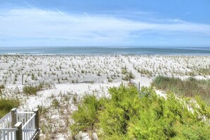 A beach with a wooden walkway leading to the water, surrounded by sand and sparse vegetation.