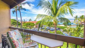 A balcony with a view of a parking lot, palm trees, and buildings in the background.