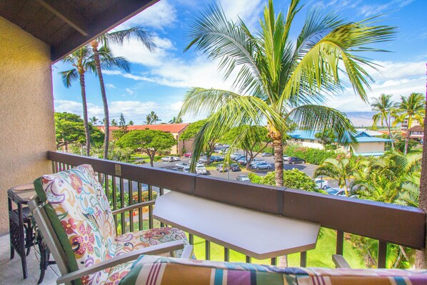 A balcony with a view of a parking lot, palm trees, and buildings in the background.