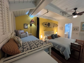 A bedroom with two beds, a ceiling fan, a surfboard decoration, and a nightstand with a lamp.