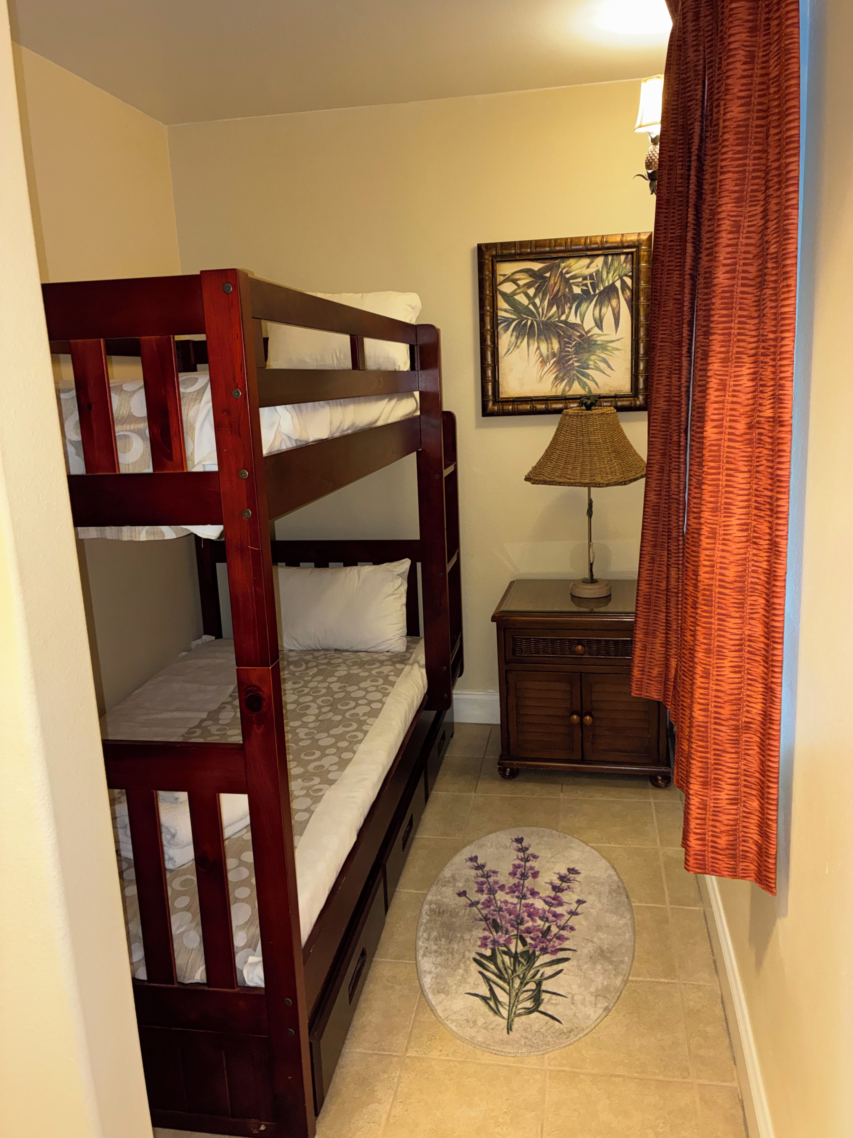 A bunk bed with a headboard, a small cabinet, a lamp, and a framed picture on the wall.