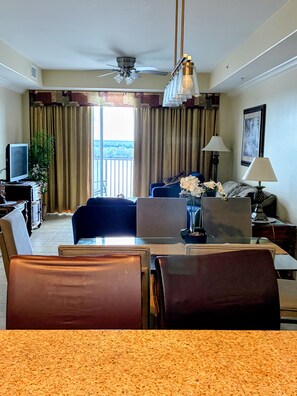 Habitación de hotel con zona de comedor, televisor, ventilador de techo y vistas al exterior.