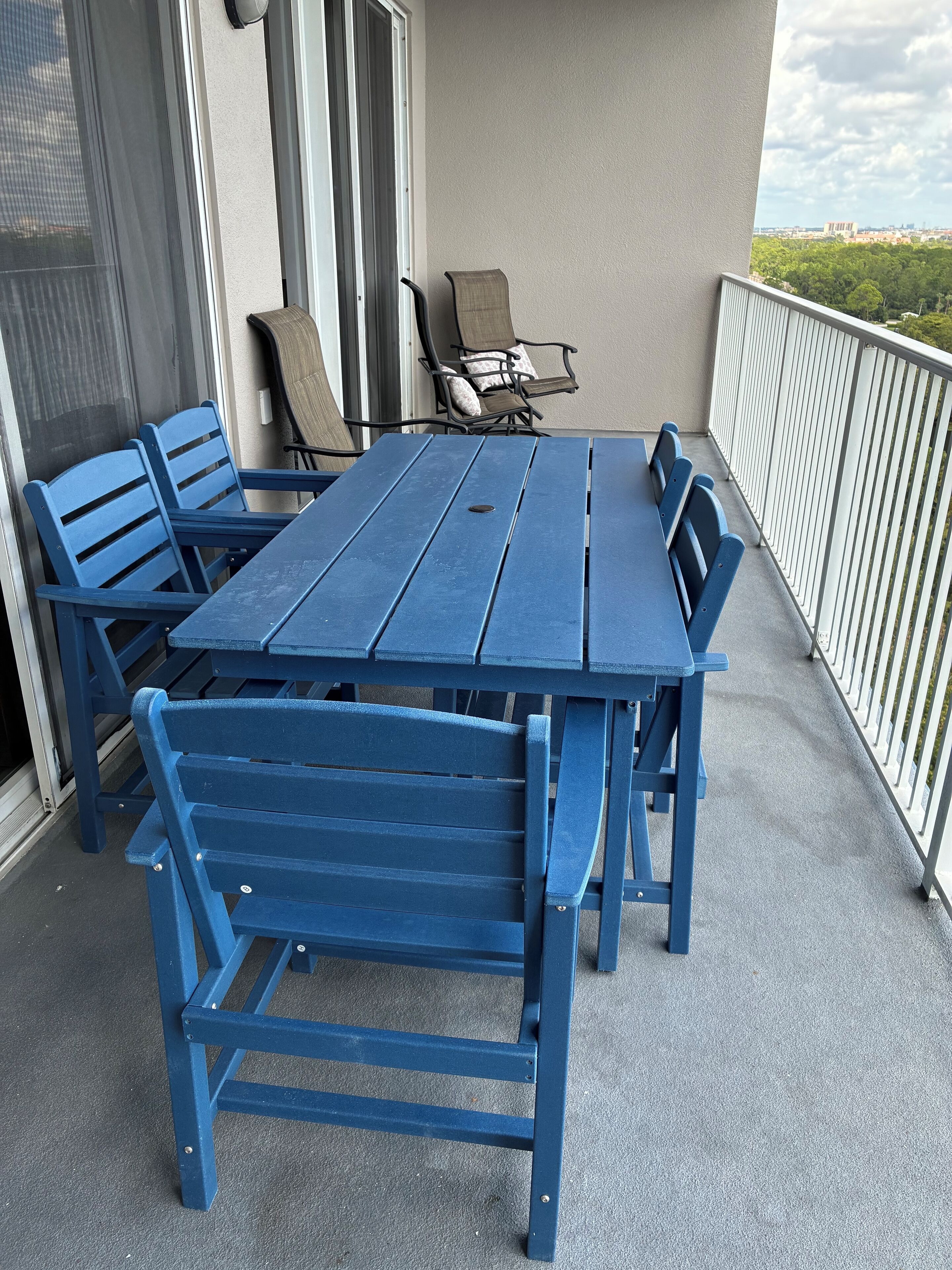 Une table et des chaises en bois bleues sur un balcon donnant sur la ville.