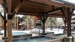 Area piscina esterna coperta con diverse vasche idromassaggio, travi in legno e bordatura in pietra.