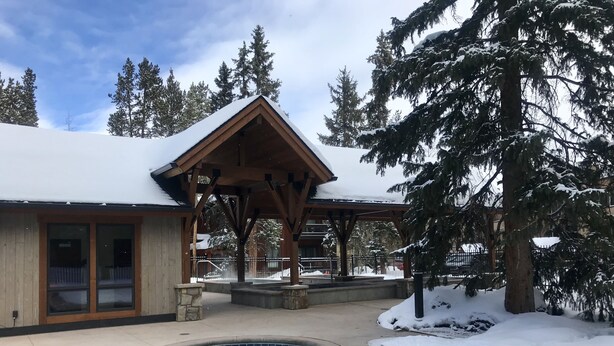 Un'area piscina con pavimento in legno, zona relax coperta e alberi innevati.