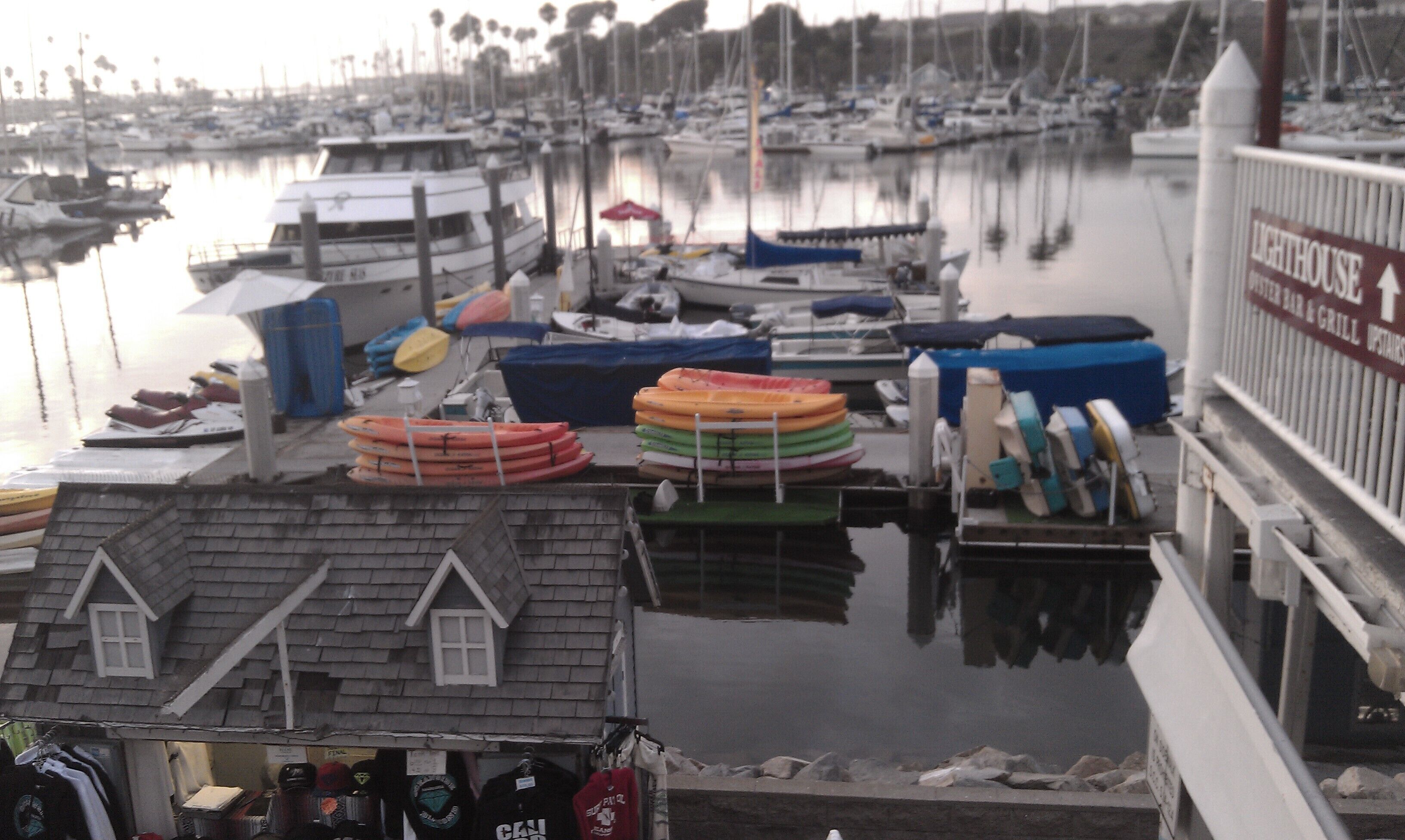 A marina with boats docked, a building with a sign reading "LIGHTHOUSE", and a small house-like structure with a window.