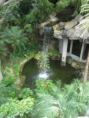 A lush garden with a small waterfall, dense foliage, and a stone structure. - Beautiful Ocean View Condo - Steps from the Beach [Pay in installments] (Oceanside)
