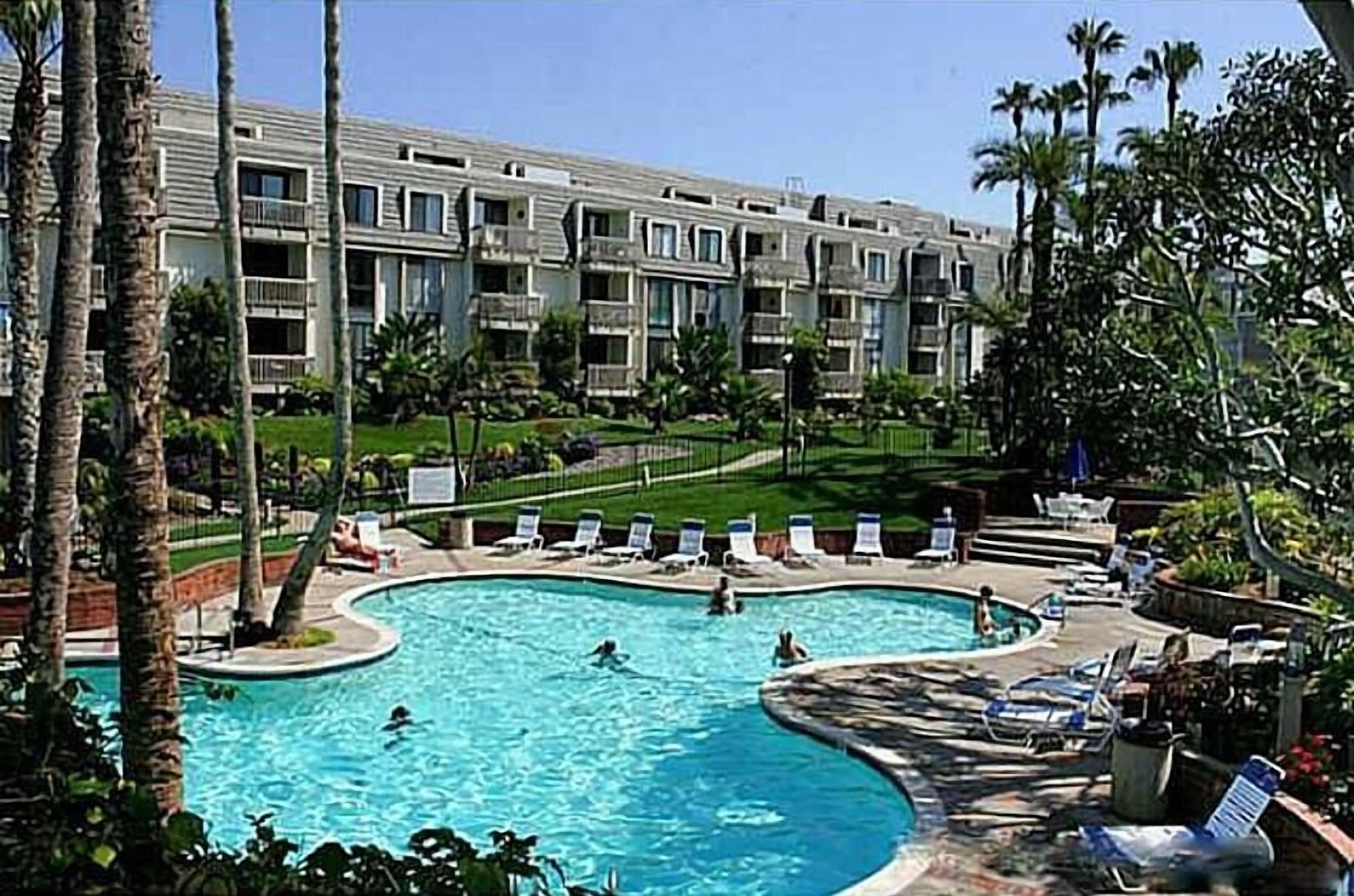 A hotel with a swimming pool surrounded by lounge chairs and palm trees.