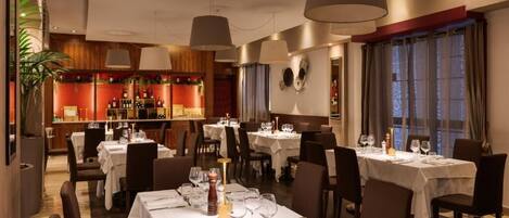 A restaurant with multiple tables set for dining, featuring a warm interior with wooden accents and pendant lighting.