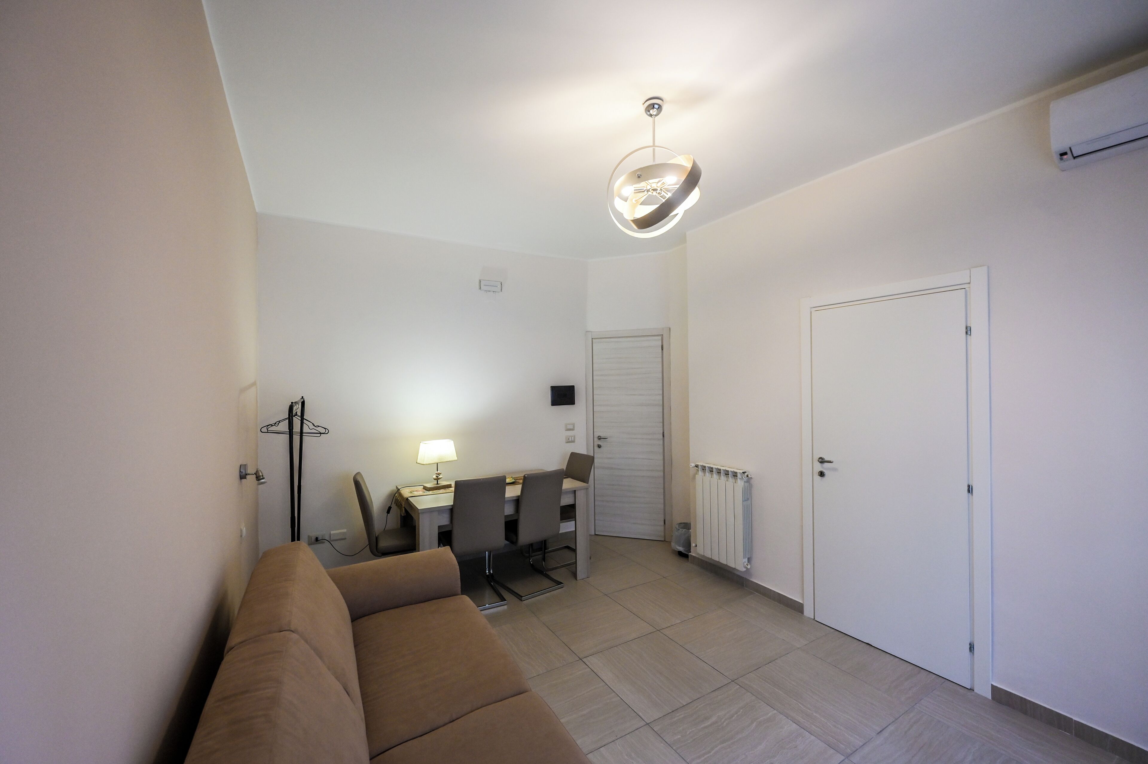A compact living space with a sofa, a dining table with chairs, a pendant light, and a closed door.