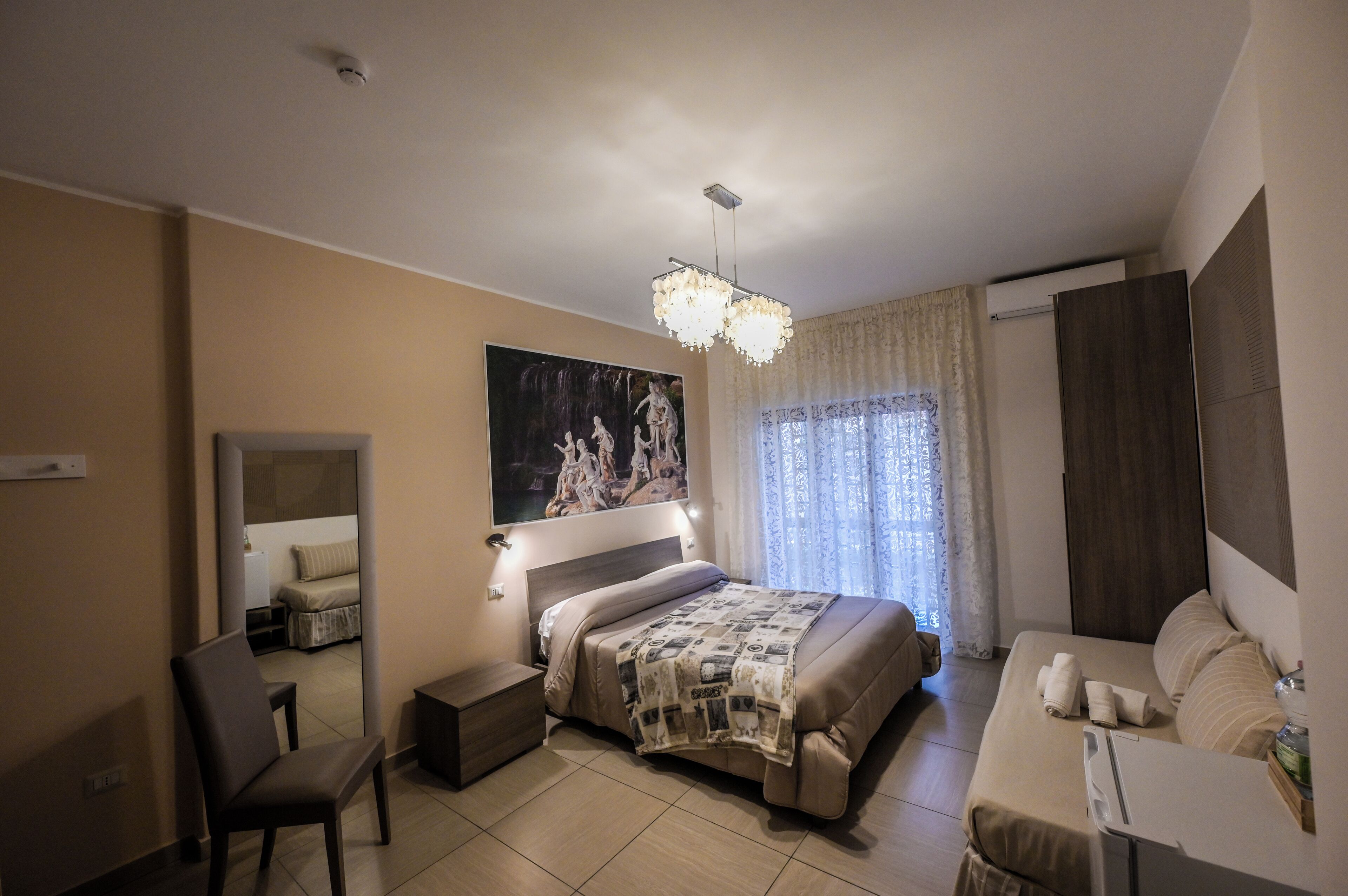 Une chambre d’hôtel comprenant un lit, une chaise, un bureau, un miroir, un tableau et un lustre.