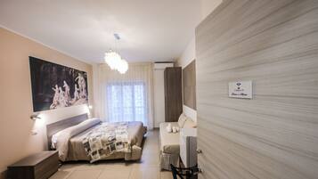 A modern hotel room with a bed, a sofa, a desk, and a large painting on the wall.