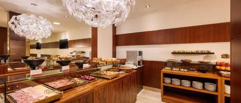Un área de bufé con distintas estaciones de comida, un mostrador de madera y elegantes lámparas de cristal.