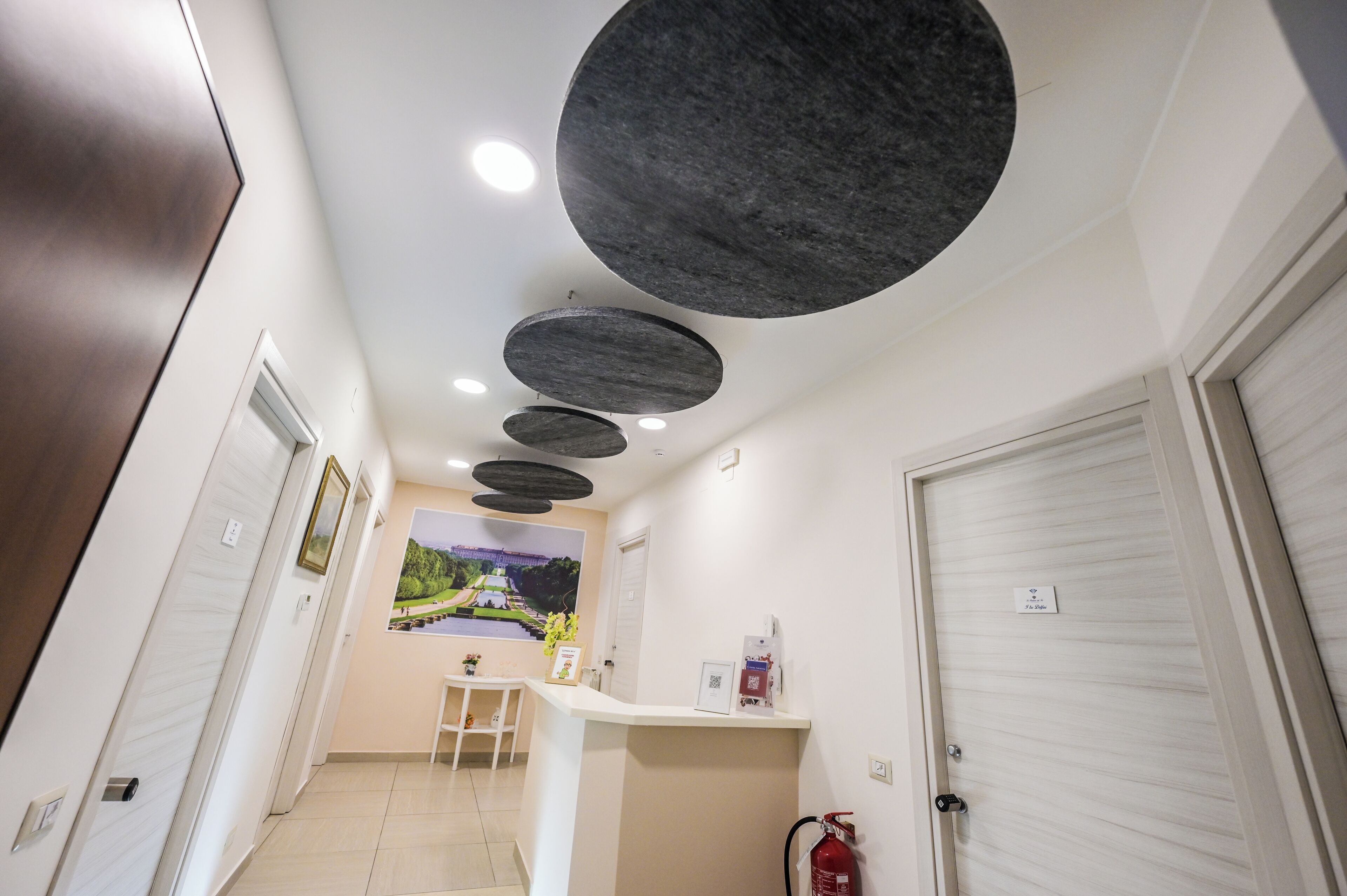 Un pasillo con mostrador de recepción, extintor y una puerta con placa.