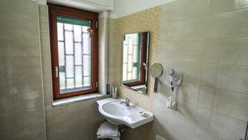 A bathroom with a sink, a window with a wooden frame, a mirror, and a hairdryer on the wall.