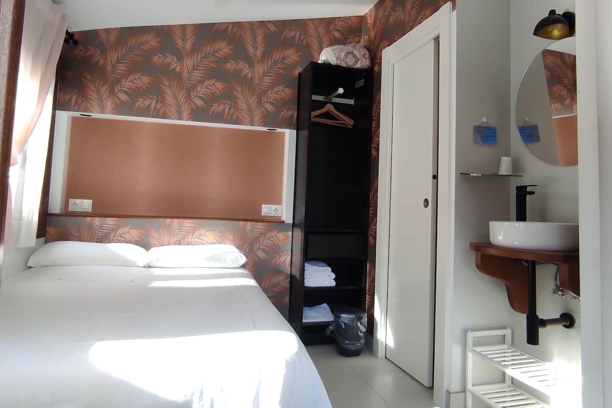 Ein Hotelzimmer mit Bett, Schrank, Bad mit Waschbecken und Spiegel sowie einem Fenster mit Vorhängen.