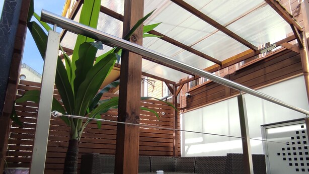 A covered outdoor area with a metal roof, wooden slats, and a seating area with wicker furniture. - Los Patios de Santander (Santander)