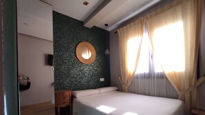 A bedroom with a bed, a wooden nightstand, a round mirror, and a wall-mounted TV. - Los Patios de Santander (Santander)