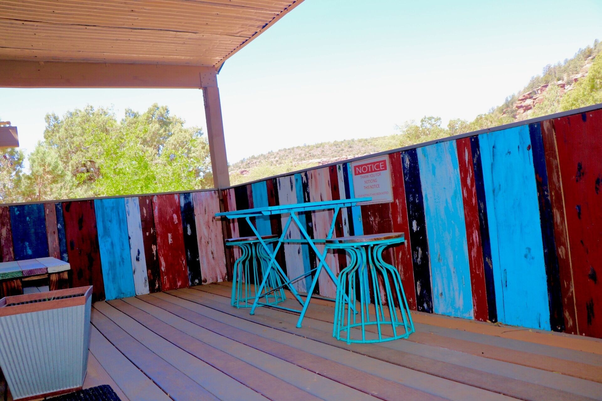A covered outdoor area with a wooden deck, a table with chairs, and a colorful painted fence.