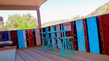 A covered outdoor area with a wooden deck, a table with chairs, and a colorful painted fence.