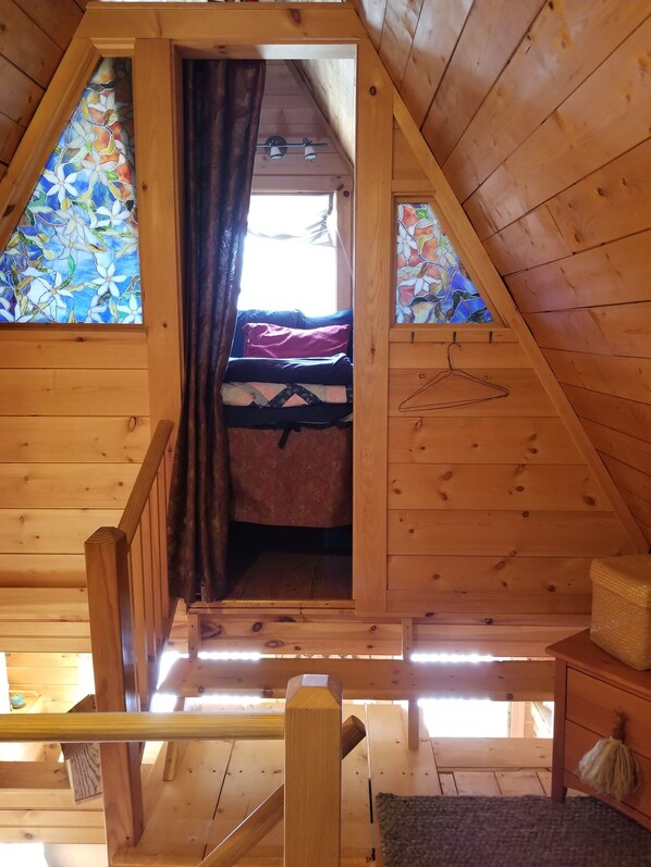 A wooden attic bedroom with a bed, a hanging chair, and a window with stained glass. - Cozy, Charming Vermont Chalet close to 5 major ski areas sleeps 4 (Stockbridge)