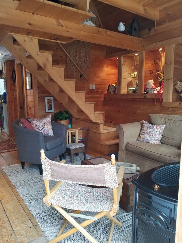 Un interior de cabaña rústica y acogedora, con una escalera de madera, un sofá, un sillón mecedora y una chimenea.