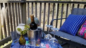 Una terraza de madera con una mesa que sostiene una botella, vasos y una bandeja.