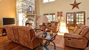 A spacious living room with a stone fireplace, leather sofas, and a star decoration on the wall. - FALL FLASH SALE-Perfect Getaway with Natural Spring Swimming Hole! (Spicewood)