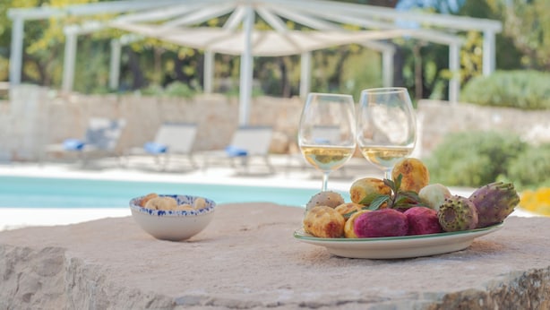 A dining table with a plate of food and two wine glasses, a bowl, and a white umbrella structure in the background. - Dimora il Mandorlo (Ostuni)