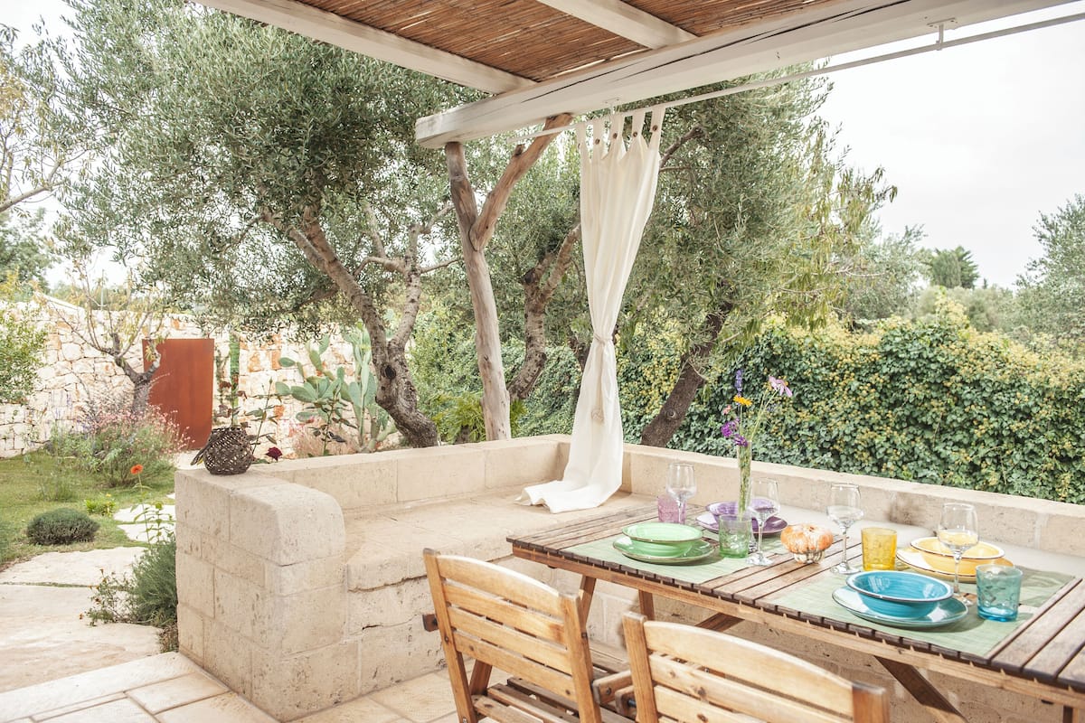 An outdoor dining area with a stone bench, wooden chairs, and a table set for two.