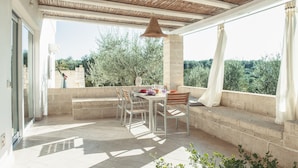 An outdoor patio with a table and chairs, a hanging light fixture, and a view of greenery. - Dimora il Mandorlo (Ostuni)