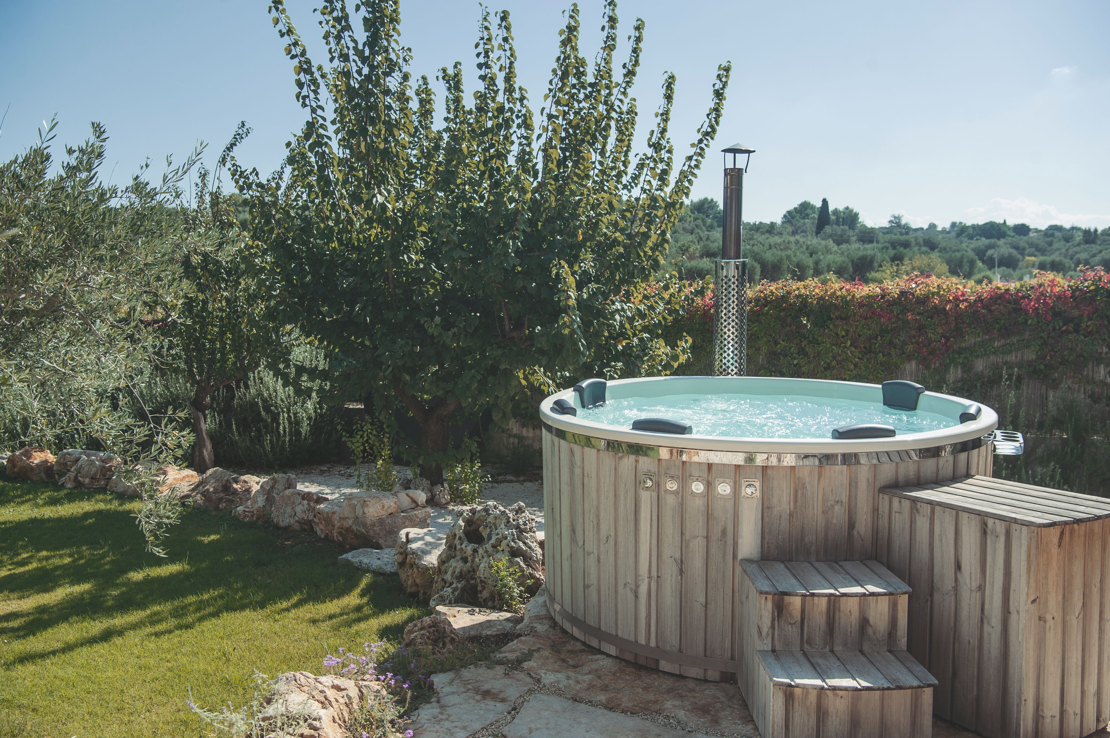 A hot tub with wooden steps and a metal structure, surrounded by a garden with rocks and trees.
